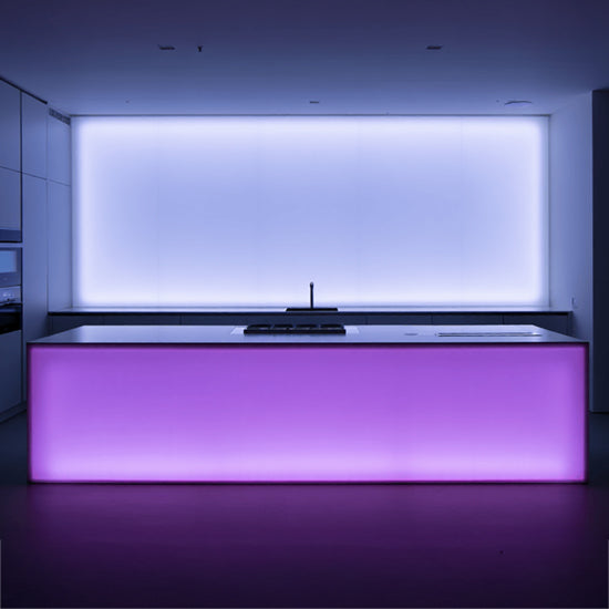 Küche mit einer Kücheninsel; an der Vorderseite der Insel eine LED-Wand mit Kanteneinstrahlung in Rosa, dahinter eine LED-Wand in Weiß mit Kanteneinstrahlung.