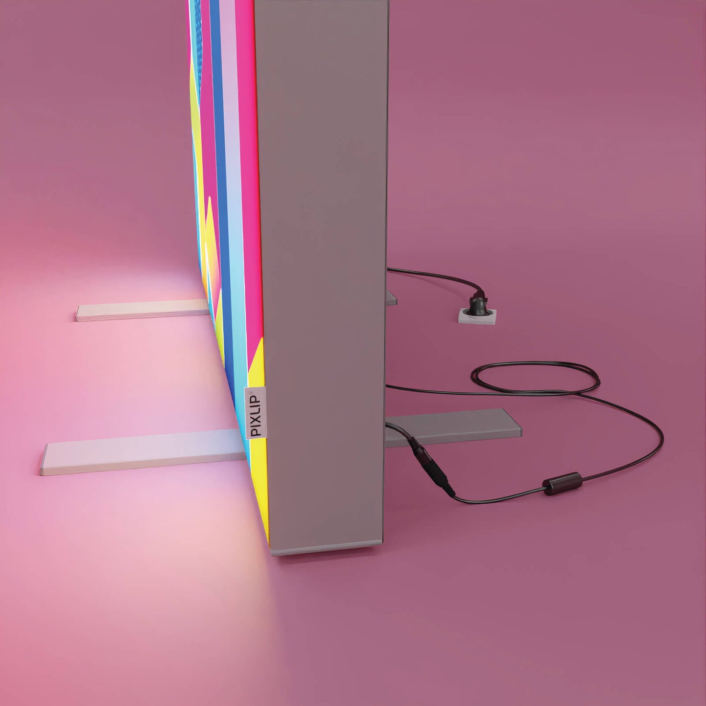 Detailansicht eines PIXLIP POP Rahmens mit angeschlossenem Netzgerät und Stromkabel, aufgestellt mit Standfüßen vor rosa Hintergrund.