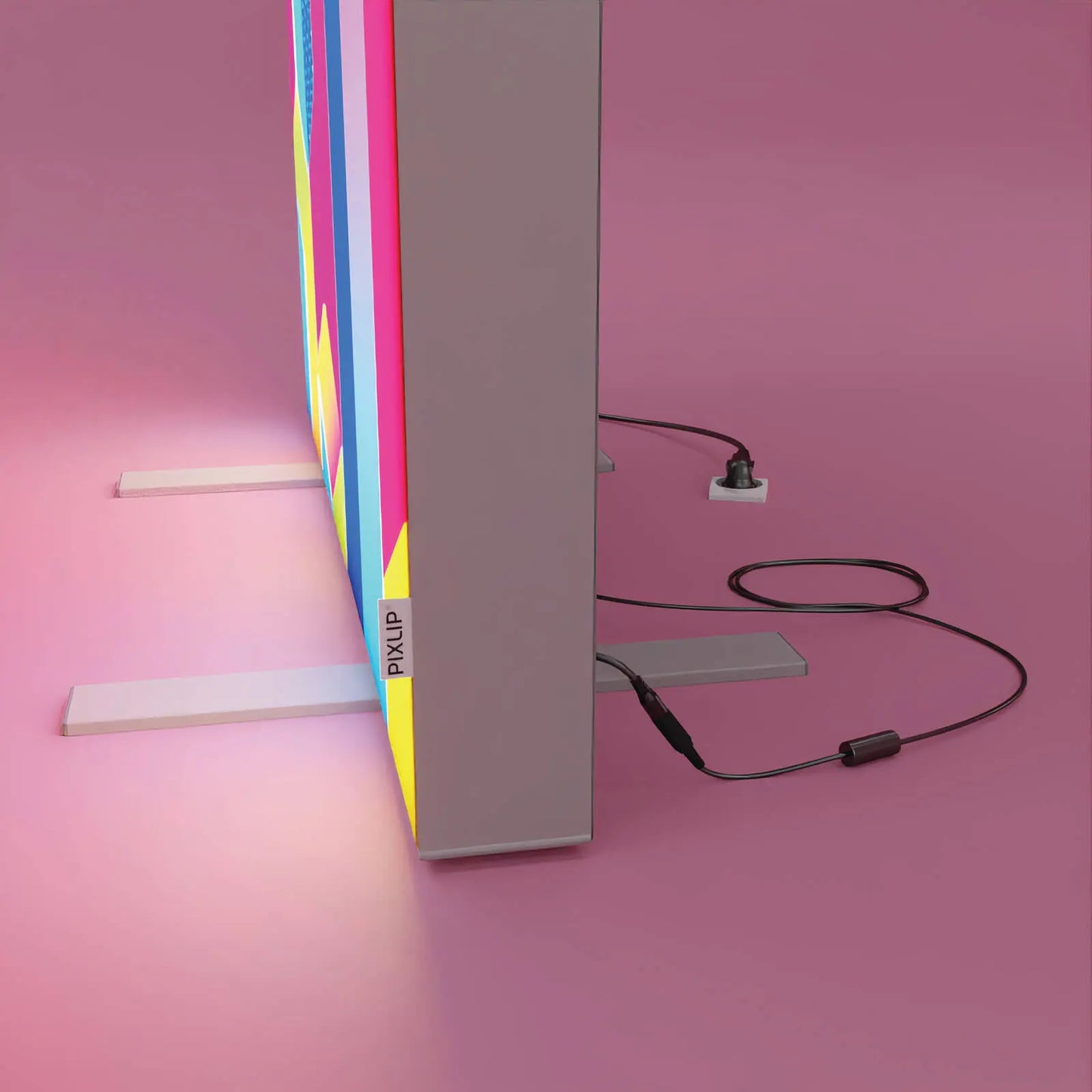 Detailansicht eines PIXLIP POP Rahmens mit angeschlossenem Netzgerät und Stromkabel, aufgestellt mit Standfüßen vor rosa Hintergrund.