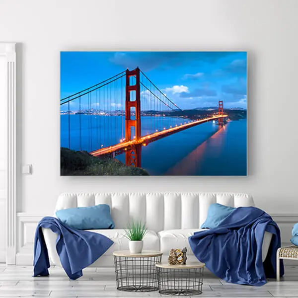 Helles, modern eingerichtetes Wohnzimmer mit blauen Akzenten; an der Wand hängt ein großes Akustikbild der Golden Gate Bridge bei Dämmerung