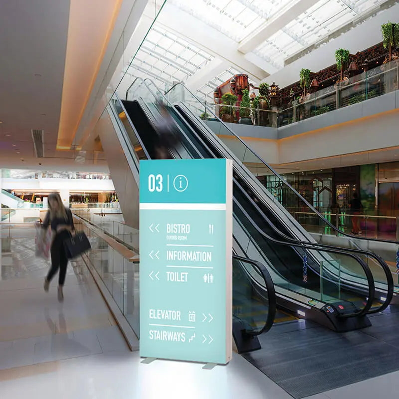 Beleuchtete PIXLIP GO Infostele von Primex mit Stoffbanner als Wegweiser im Einkaufszentrum, platziert neben einer Rolltreppe für optimale Orientierung.