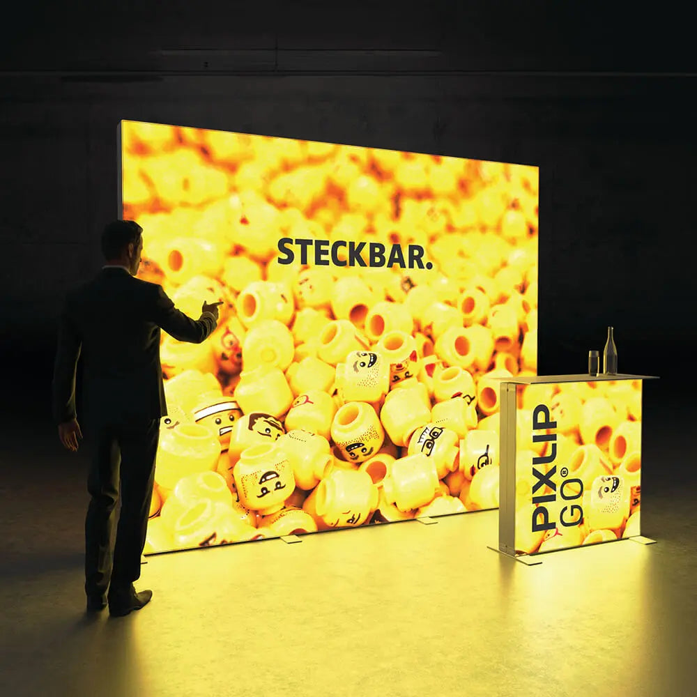 Beleuchteter PIXLIP GO Messestand mit modularer Rückwand und passender Theke in leuchtendem Gelb mit Stoffbanner .