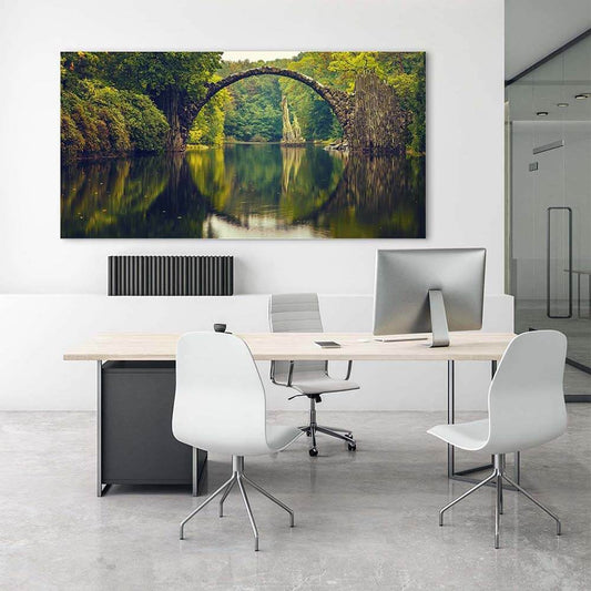 Rechteckiges Akustikbild der Rakotzbrücke mit Spiegelung im Wasser, hinter einem Schreibtisch