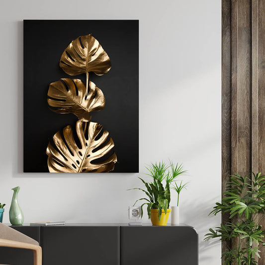 Rechteckiges schwarzes Akustikbild mit 3 goldenen Monsterablättern über einem Sideboard