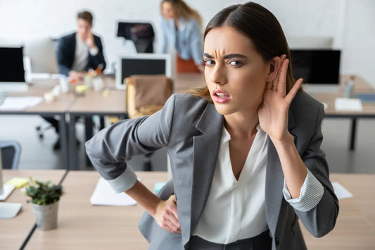 Eine Frau beugt sich nach vorner und hält eine Hand an ihr Ohr, damit sie besser hört.
