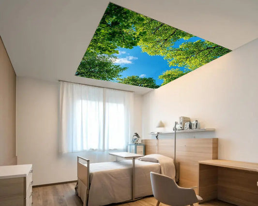 Über dem Bett in einem Seniorenzimmer hängt die Primex Lichtdecke 55 mm mit Flächenlicht und eröffnet durch ein Baumwipfelmotiv einen Blick in den Himmel