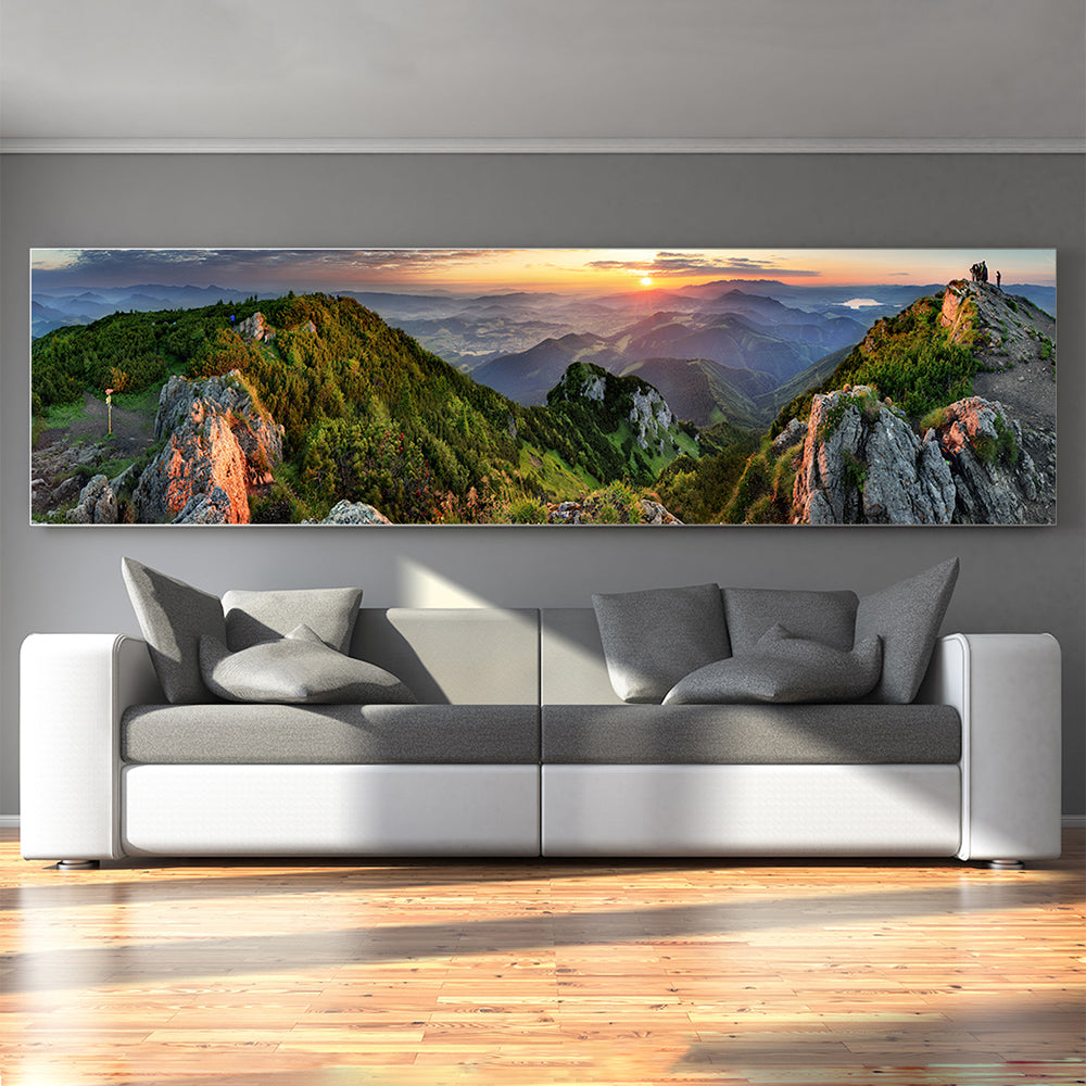 Modernes Wohnzimmer mit grauem Sofa; darüber hängt ein breites Panorama-Akustikwandbild, das eine grüne Berglandschaft bei Sonnenuntergang zeigt.