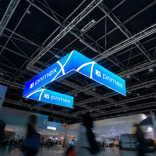 Leuchtender LED-Deckenhänger in U-Form mit blauem Branding hängt über einer Messehalle mit modernem Stahlträger-Dach und Besuchern darunter.