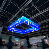 Quadratischer LED-Deckenhänger mit blauem Primex-Logo, der an einer Metallträger-Konstruktion in einer Messehalle befestigt ist.