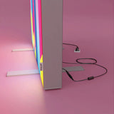 Detailansicht eines PIXLIP POP Rahmens mit angeschlossenem Netzgerät und Stromkabel, aufgestellt mit Standfüßen vor rosa Hintergrund.