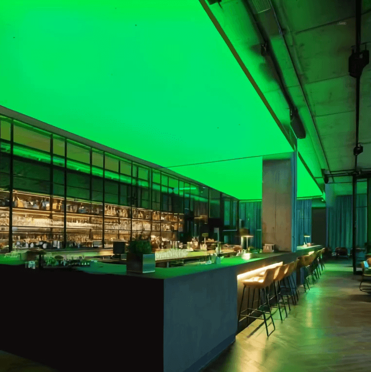Moderne Bar mit langen Theken und Barhockern, an der Decke eine großflächige RGBW-LED-Lichtdecke, die den Raum in kräftigem Grün beleuchtet.