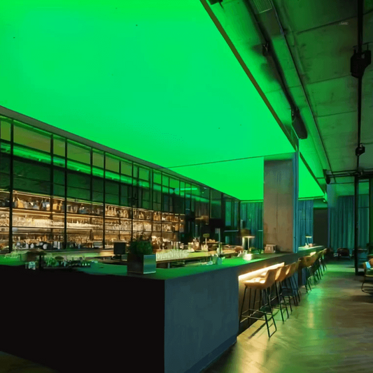Moderne Bar mit langen Theken und Barhockern, an der Decke eine großflächige RGBW-LED-Lichtdecke, die den Raum in kräftigem Grün beleuchtet.