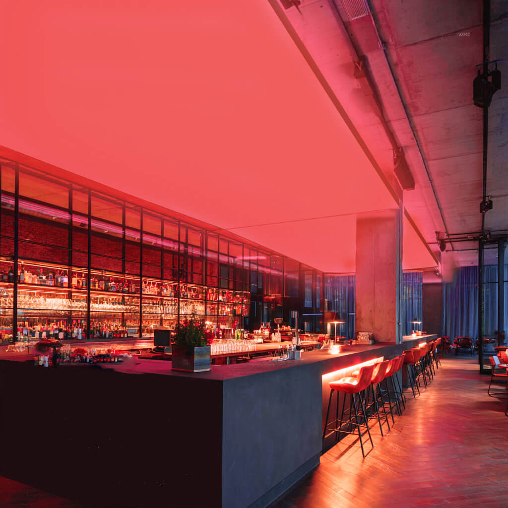 Moderne Bar mit langen Theken und Barhockern, an der Decke eine großflächige RGBW-LED-Lichtdecke, die den Raum in kräftigem Rot beleuchtet.