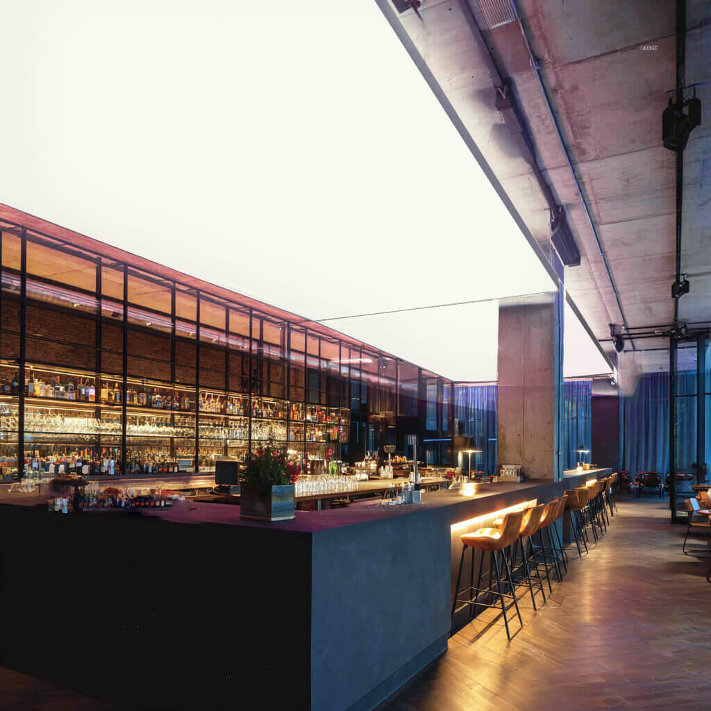 Moderne Bar mit langen Theken und Barhockern, an der Decke eine großflächige RGBW-LED-Lichtdecke, die den Raum in kräftigem Weiß beleuchtet.