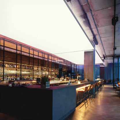 Moderne Bar mit langen Theken und Barhockern, an der Decke eine großflächige RGBW-LED-Lichtdecke, die den Raum in kräftigem Weiß beleuchtet.