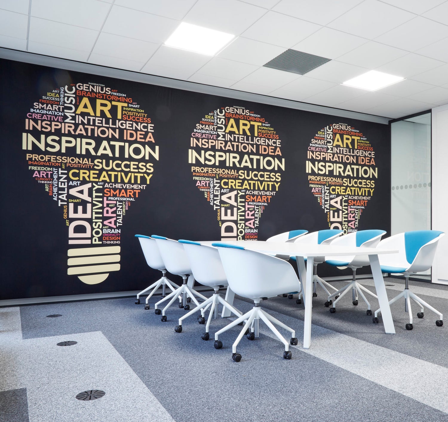 Moderner Meetingraum mit weißem Tisch und blauen Stühlen; an der schwarzen Akustikwand sind drei große Glühbirnen aus Wörtern gestaltet