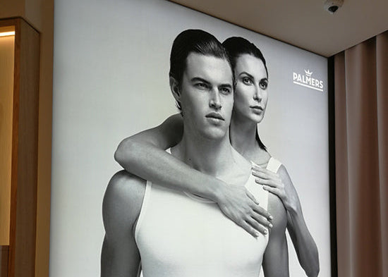 LED-Lightbox im Retailbereich für Palmers-Werbung mit einem schwarz-weißen Bild, auf dem ein Mann von hinten von einer Frau umarmt wird.