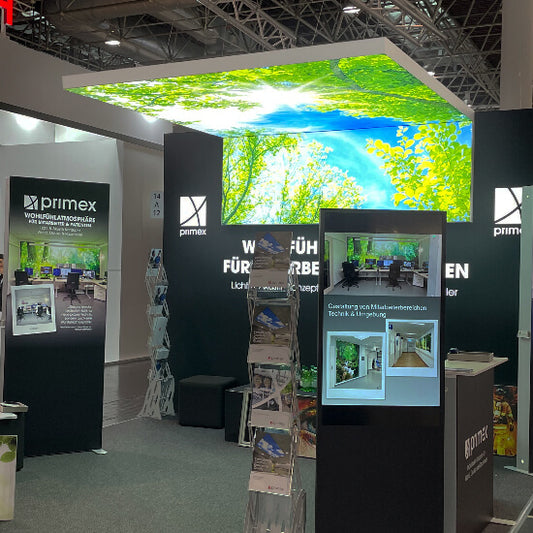 LED-Messehänger in L-Form mit hinterleuchtetem Textildruck; das Motiv zeigt blauen Himmel und grüne Baumkronen, wodurch eine offene und natürliche Atmosphäre entsteht.