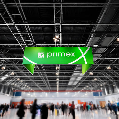 Messehalle mit einem großen, grünen, unbeleuchteten Deckenhänger in U-Form, der das weiße Logo und den Schriftzug „primex“ zeigt. Im Hintergrund sind Menschen und Messestände zu sehen.