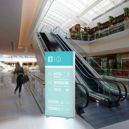 Beleuchtete PIXLIP GO Infostele von Primex mit Textildruck als Wegweiser im Einkaufszentrum, platziert neben einer Rolltreppe für optimale Orientierung.