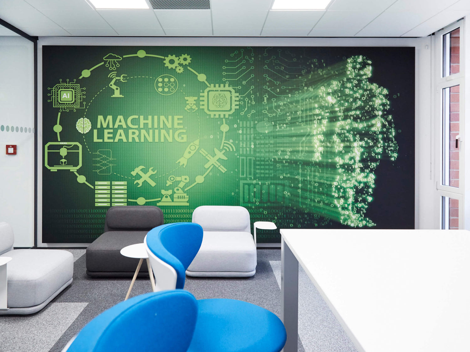Moderner Besprechungsbereich mit farbigen Sitzmöbeln; an der Wand großes Akustikbild mit grünem „Machine Learning“-Motiv, digitalen Symbolen und einer Figur aus leuchtenden Datenpunkten.