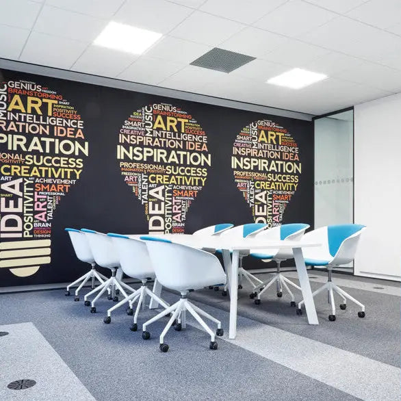 Moderner Besprechungsraum mit weißen Tischen und blauen Stühlen, an der Wand ein Akustikbild mit  drei große Glühbirnen-Grafiken aus bunten Wortwolken mit Begriffen wie Inspiration, Idee und Kreativität.