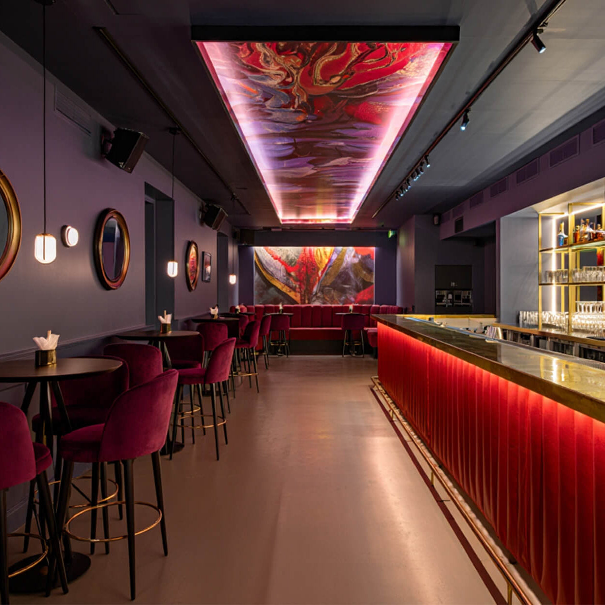 Moderner Gastrobereich mit Sitzgruppen und einer großflächigen LED-Lichtdecke, die ein abstraktes Motiv in intensiven Rottönen zeigt.
