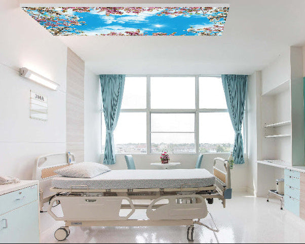 Helles Patientenzimmer mit einer LED-Lichtdecke, die einen blauen Himmel mit Kirschblüten zeigt und eine freundliche, beruhigende Atmosphäre schafft.