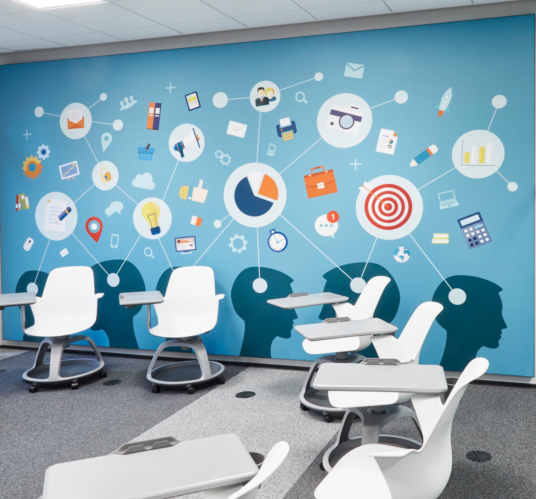 In einem Besprechungsraum mit Stuhlkreis hängt ein XXL-Akustikbild. Das Motiv ist in Blautönen gestaltet und zeigt am unteren Rand mehrere Menschenköpfe, aus denen unterschiedliche Ideen und Gedanken abgeleitet werden.