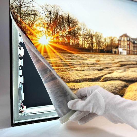 Darstellung eines Textildrucks mit LED-Kanteneinstrahlung, während das Textil unten vom Spannrahmenprofil abgezogen wird; die LED-Technik ist sichtbar.